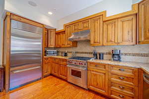 Kitchen featuring light stone countertops, premium appliances, light hardwood / wood-style flooring, and backsplash