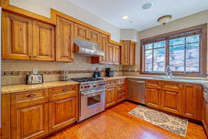 Kitchen with sink, stainless steel appliances, tasteful backsplash, light stone counters, and light wood-type flooring