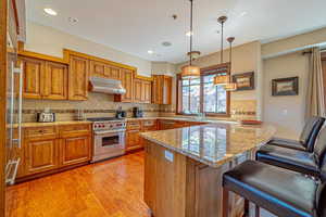 Kitchen with light stone counters, stainless steel appliances, decorative light fixtures, light hardwood / wood-style flooring, and a breakfast bar area