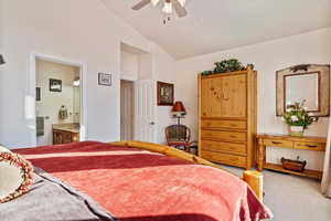 Carpeted bedroom with ensuite bathroom, ceiling fan, and lofted ceiling