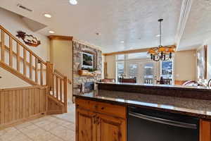 Kitchen featuring granite counters, a textured ceiling, dishwasher, a stone fireplace, and hanging light fixtures