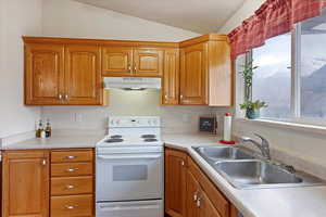 Kitchen featuring a textured ceiling, vaulted ceiling, white electric stove, and sink