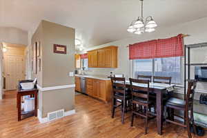 Kitchen with light wood-type flooring, stainless steel dishwasher, sink, decorative light fixtures, and a chandelier