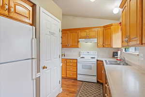 Kitchen featuring light wood-type flooring, a textured ceiling, white appliances, vaulted ceiling, and sink