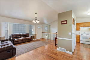 Living room with light hardwood / wood-style flooring, a chandelier, and lofted ceiling