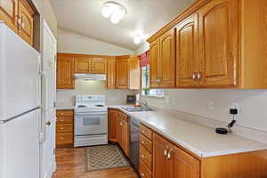 Kitchen featuring sink, dark wood-type flooring, vaulted ceiling, a textured ceiling, and white appliances