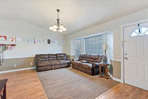 Living room featuring hardwood / wood-style flooring, vaulted ceiling, and an inviting chandelier