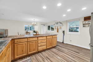 Kitchen with an inviting chandelier, light hardwood / wood-style flooring, stainless steel fridge, decorative light fixtures, and kitchen peninsula