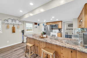 Kitchen featuring a kitchen bar, kitchen peninsula, light stone counters, and stainless steel appliances