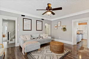 Living room with ceiling fan, dark hardwood / wood-style floors, a textured ceiling, and ornamental molding