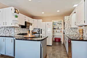 Kitchen with white refrigerator with ice dispenser, white cabinets, sink, tasteful backsplash, and kitchen peninsula