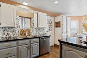 Kitchen with sink, stainless steel dishwasher, backsplash, gray cabinets, and white cabinets