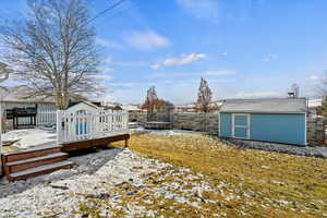 Snowy yard with a wooden deck, a storage unit, and a trampoline