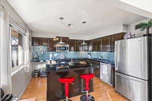 Kitchen with a kitchen breakfast bar, dark brown cabinets, stainless steel appliances, light hardwood / wood-style flooring, and a kitchen island