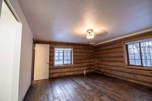 Spare room featuring rustic walls, dark wood-type flooring, and a textured ceiling