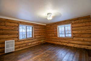 Spare room with a textured ceiling, rustic walls, and dark wood-type flooring