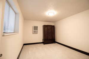 Carpeted spare room featuring a textured ceiling and heating unit