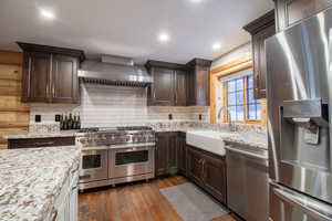 Kitchen featuring light stone countertops, dark hardwood / wood-style flooring, wall chimney exhaust hood, stainless steel appliances, and sink