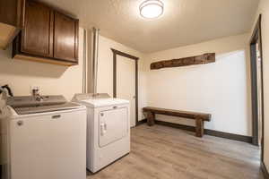 Laundry room featuring cabinets, a textured ceiling, light hardwood / wood-style flooring, and washing machine and clothes dryer