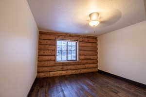 Unfurnished room with a textured ceiling, dark hardwood / wood-style flooring, and rustic walls