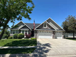 Craftsman-style house featuring stone siding, driveway, a front lawn, and an attached garage