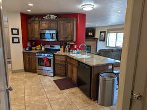 Kitchen featuring a textured ceiling, sink, appliances with stainless steel finishes, and a tiled fireplace