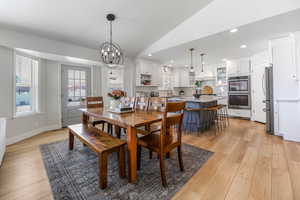 Dining area with light wood-type flooring, lofted ceiling, sink, and an inviting chandelier