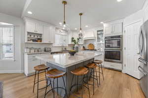 Kitchen with premium range hood, light stone countertops, decorative light fixtures, white cabinetry, and stainless steel appliances