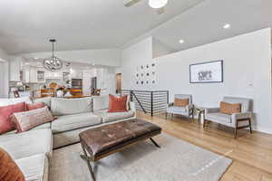 Living room featuring ceiling fan with notable chandelier, lofted ceiling, sink, and light hardwood / wood-style flooring