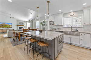 Kitchen featuring lofted ceiling, white cabinets, sink, hanging light fixtures, and tasteful backsplash