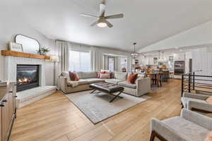 Living room featuring a fireplace, ceiling fan with notable chandelier, light hardwood / wood-style flooring, and lofted ceiling