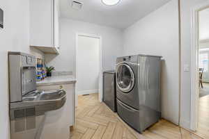 Laundry area with washer and dryer, cabinets, and light parquet floors