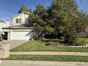 View of property hidden behind natural elements featuring a front lawn and a garage