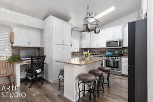 Kitchen with a breakfast bar, stainless steel appliances, vaulted ceiling, a kitchen island, and white cabinetry