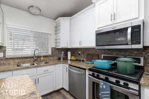 Kitchen featuring light stone countertops, decorative backsplash, stainless steel appliances, sink, and white cabinetry