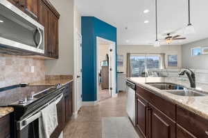 Kitchen with pendant lighting, sink, tasteful backsplash, light stone counters, and stainless steel appliances