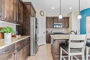 Kitchen featuring tasteful backsplash, light stone counters, hanging light fixtures, and stainless steel appliances