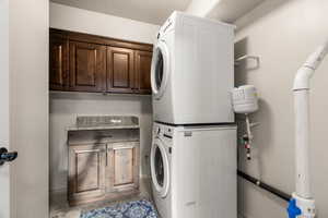 Washroom featuring stacked washer and dryer and cabinets