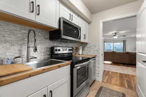 Kitchen with appliances with stainless steel finishes, backsplash, sink, white cabinets, and light tile patterned flooring