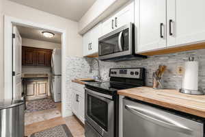 Kitchen featuring white cabinets, wood counters, appliances with stainless steel finishes, and stacked washer and clothes dryer