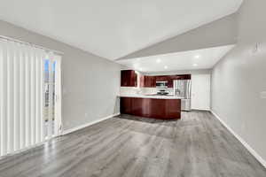 Kitchen with appliances with stainless steel finishes, lofted ceiling, light hardwood / wood-style floors, and kitchen peninsula