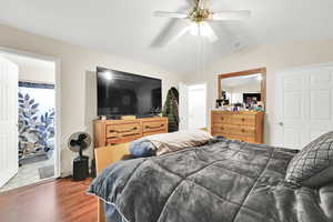 Bedroom with dark hardwood / wood-style flooring, ensuite bathroom, vaulted ceiling, and ceiling fan