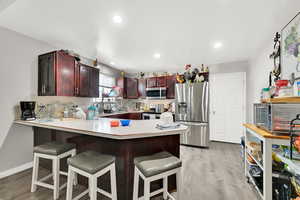 Kitchen featuring kitchen peninsula, backsplash, stainless steel appliances, light hardwood / wood-style floors, and a breakfast bar area