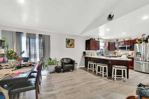 Kitchen with lofted ceiling, light wood-type flooring, appliances with stainless steel finishes, a kitchen bar, and kitchen peninsula