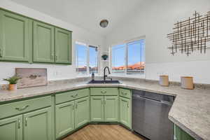 Kitchen with light wood-type flooring, vaulted ceiling, sink, green cabinetry, and dishwasher