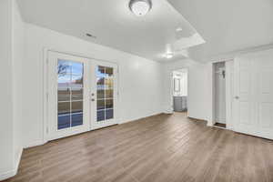 Unfurnished bedroom featuring access to exterior, french doors, light wood-type flooring, ensuite bath, and a textured ceiling