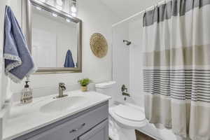 Full bathroom with vanity, shower / bathtub combination with curtain, and toilet