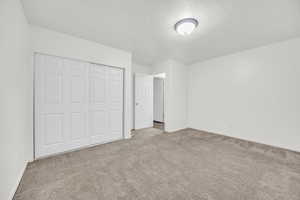 Unfurnished bedroom with a textured ceiling, light carpet, and a closet