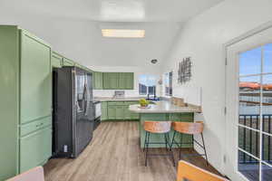 Kitchen featuring kitchen peninsula, stainless steel fridge, lofted ceiling, a kitchen bar, and green cabinetry