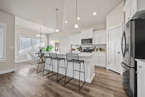 Kitchen featuring appliances with stainless steel finishes, decorative light fixtures, white cabinetry, and a center island with sink